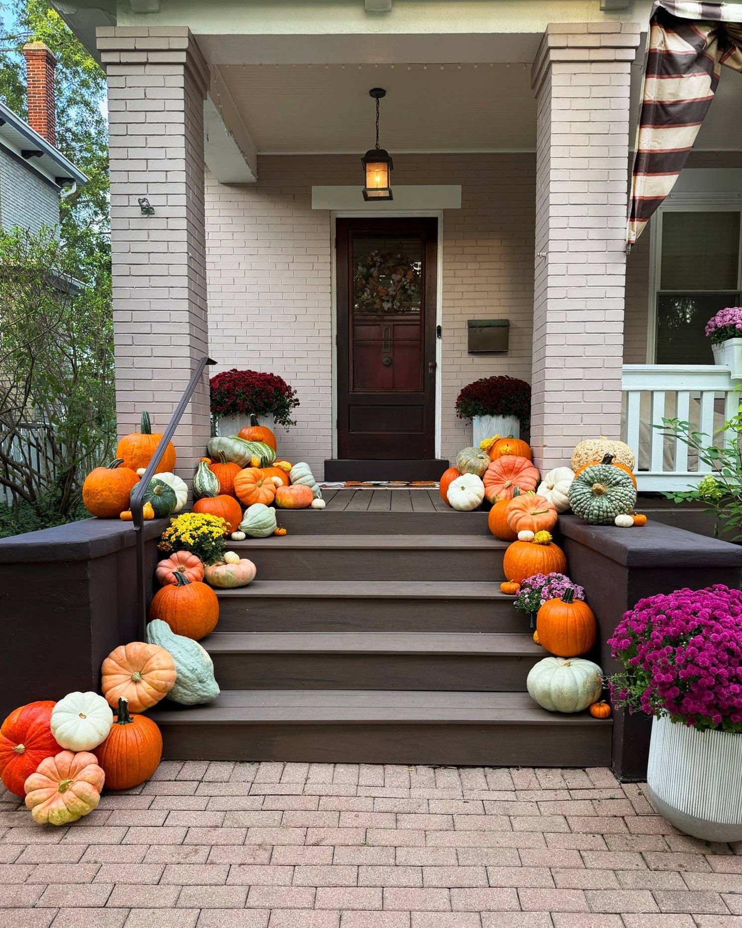 The Envy at a Mount Lookout porch: orange, white, green and heirloom pumpkins down both sides of the steps, burgundy mums beside the front door and magenta mums in a white planter