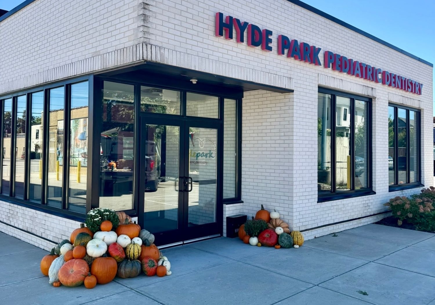 The corner entrance of Hyde Park Pediatric Dentistry in Oakley, with pumpkin, gourd and mum groupings on both sides of the glass doors