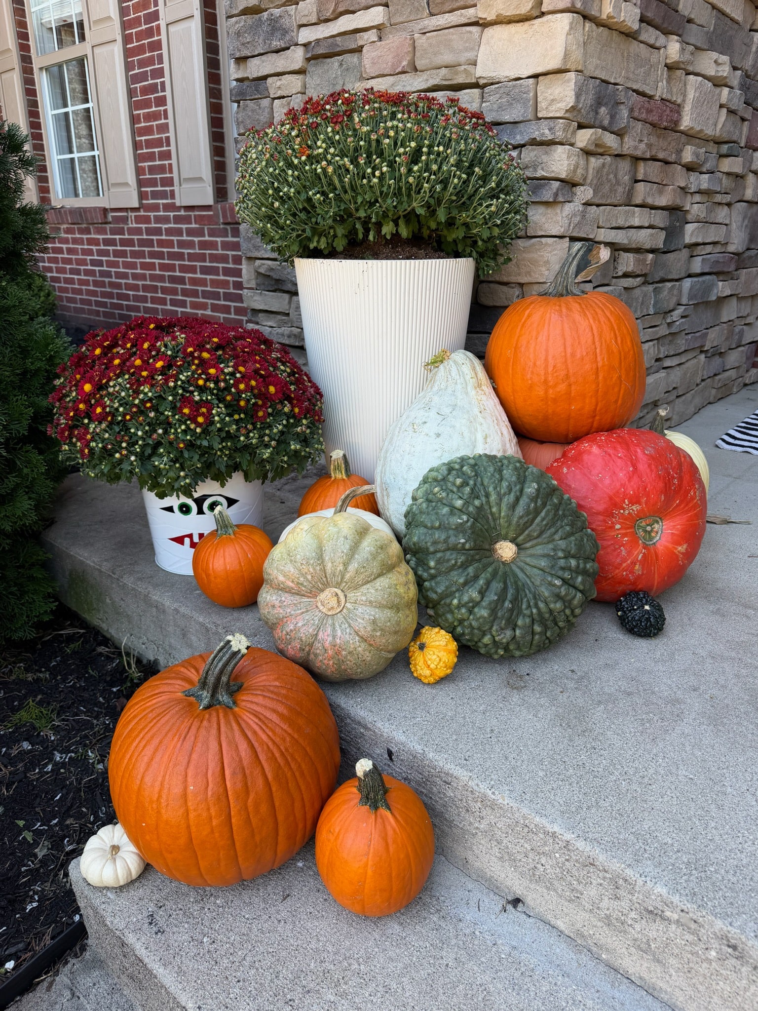 Orange and heirloom pumpkins beside red mums and a white planter at the stone entrance