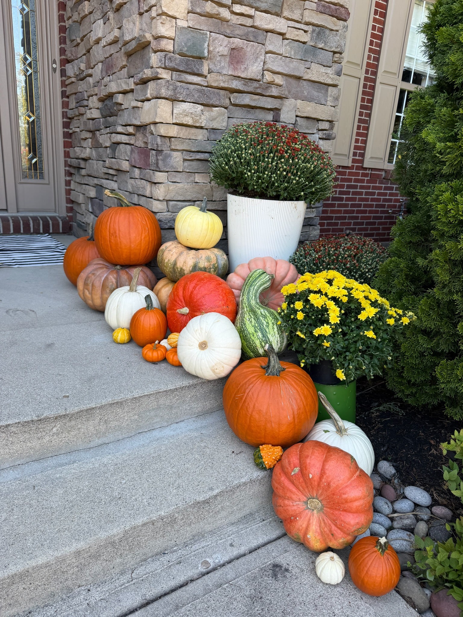 Orange, pink and white pumpkins with yellow mums along the right side of the stone entrance