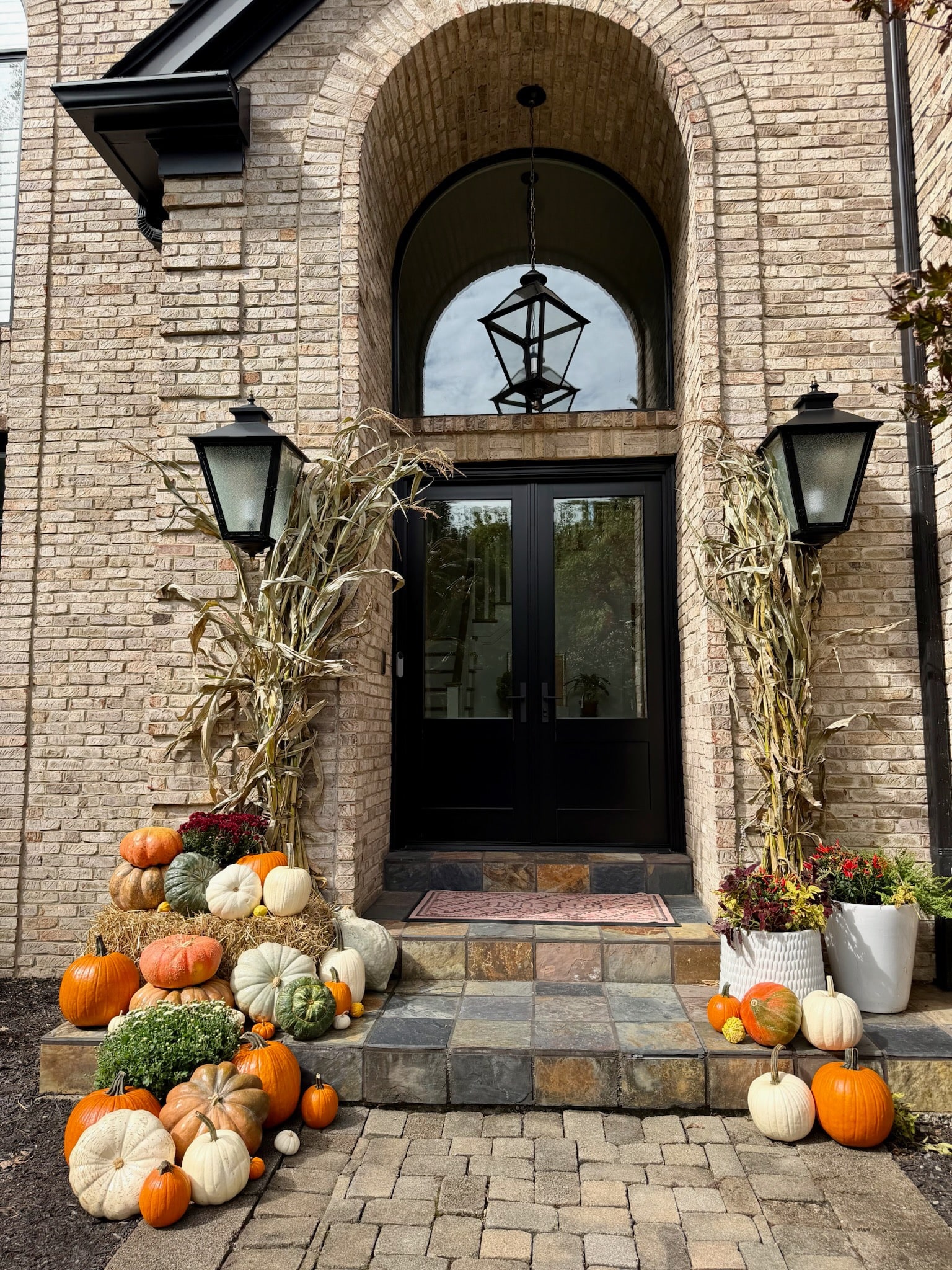 Brick entrance framed with cornstalks, with pumpkins and mums arranged on both sides of the steps