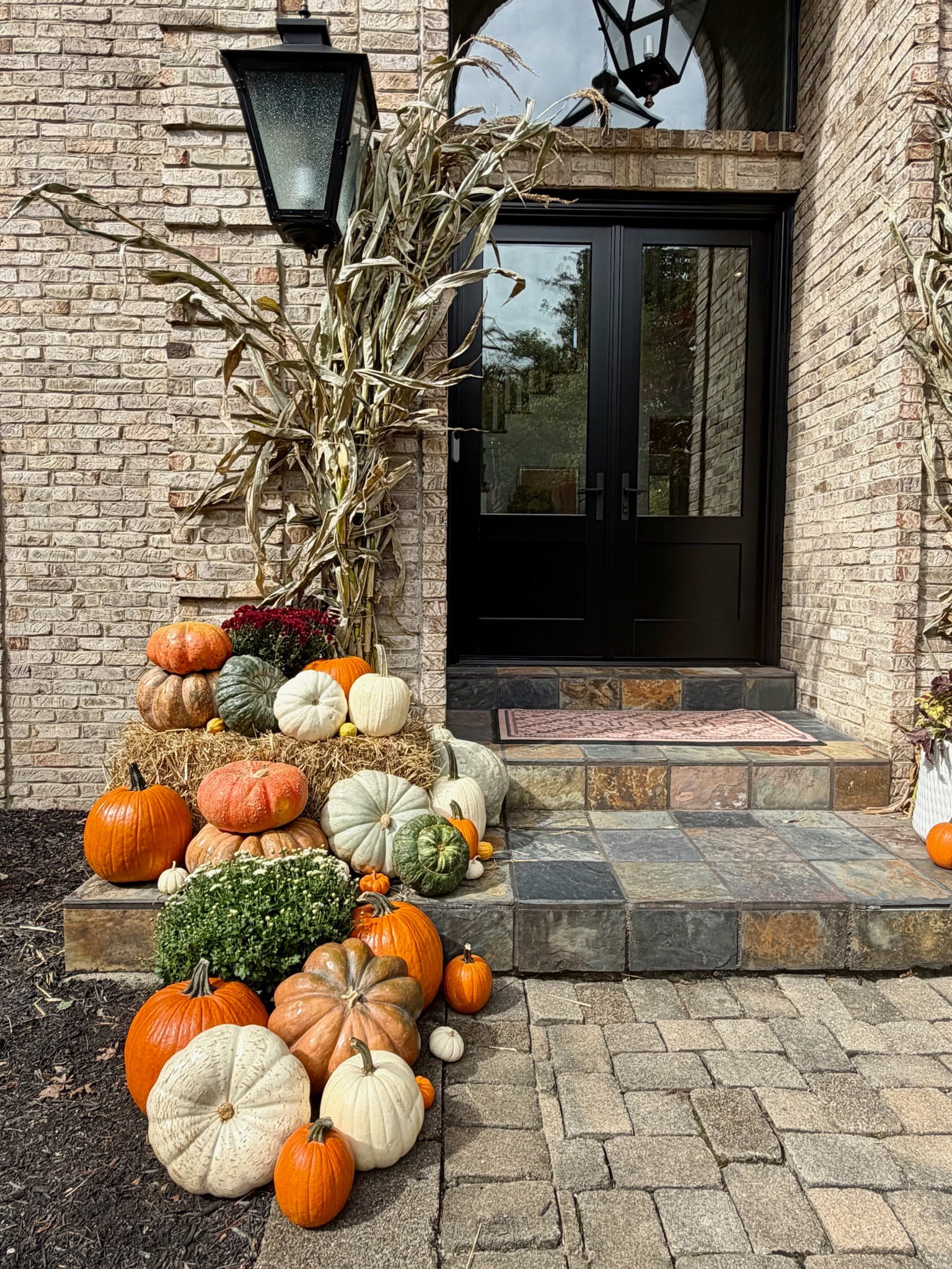 Stacked pumpkins, mums and a straw bale beside the left cornstalk bundle