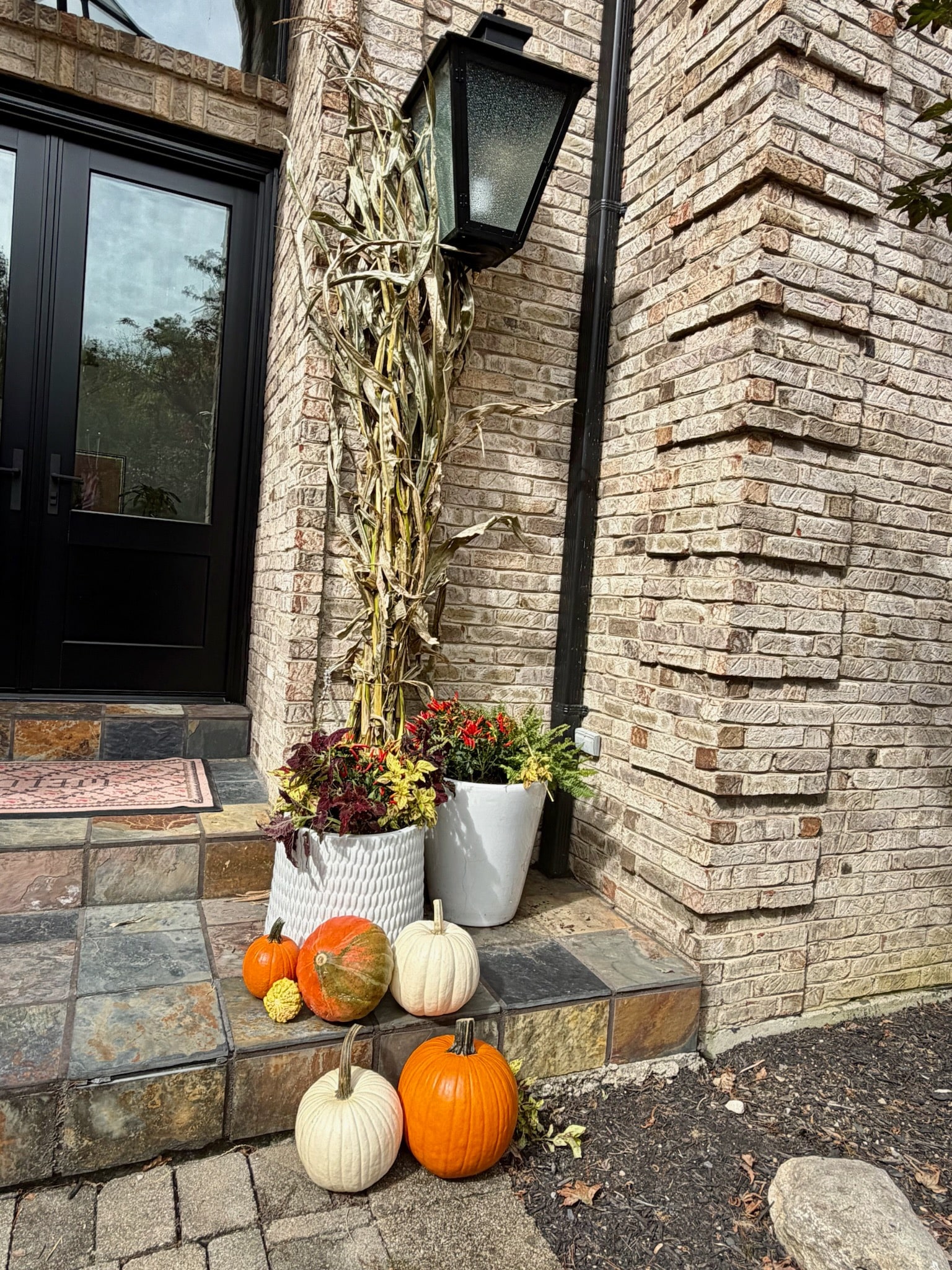 White planters, pumpkins and a cornstalk bundle at the right side of the entrance