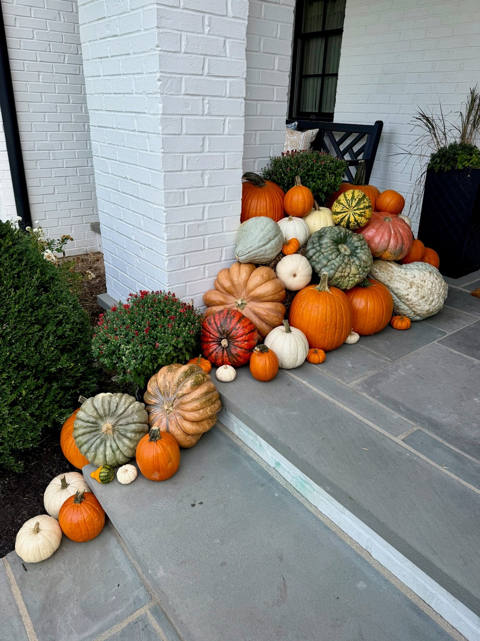 Orange, white and heirloom pumpkins with mums grouped around a white brick column and down one side of the steps