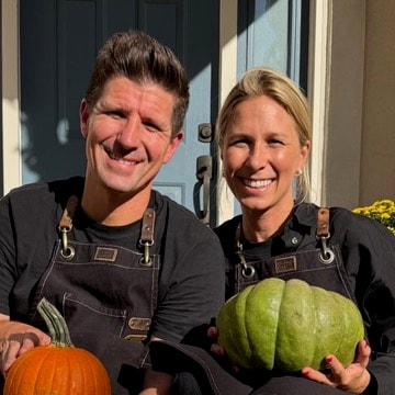 Nikki and Kyle in work aprons, smiling on the front steps of a styled porch