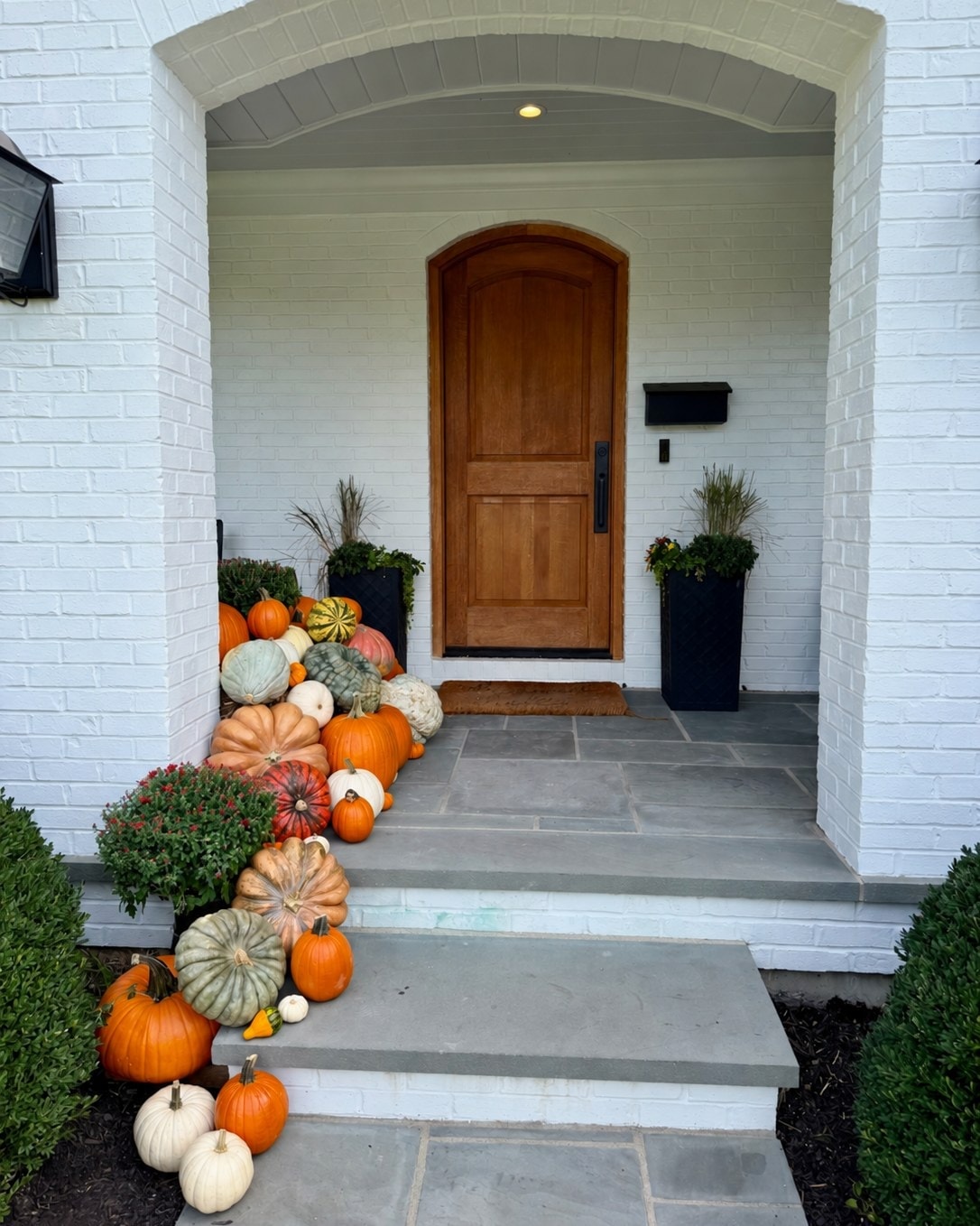 The Statement at a Mount Lookout entrance: pumpkins, gourds and mums cascade down one side of the stone steps beside a white brick archway