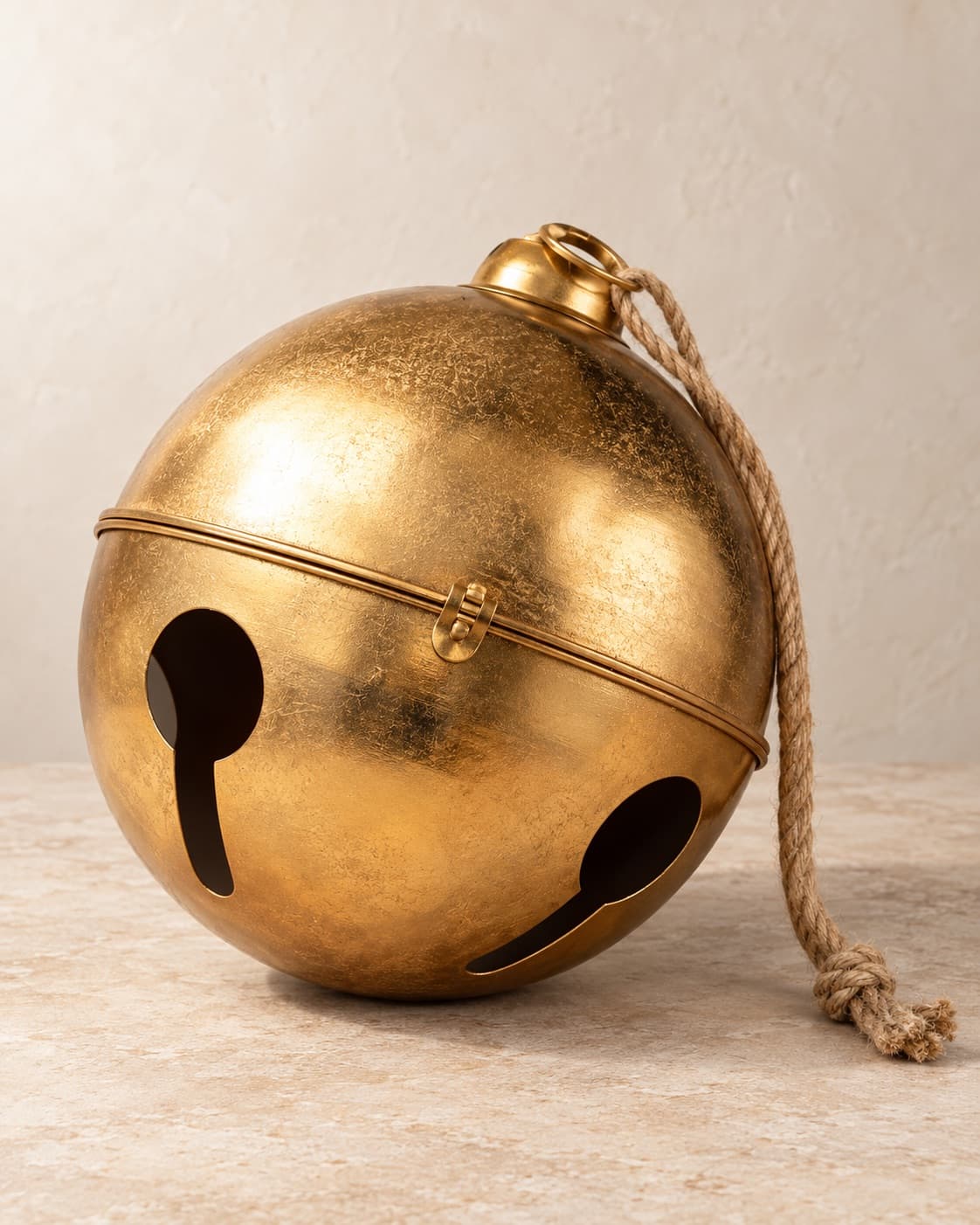 A 20-inch gold jingle bell with a jute rope tie on a pale stone floor