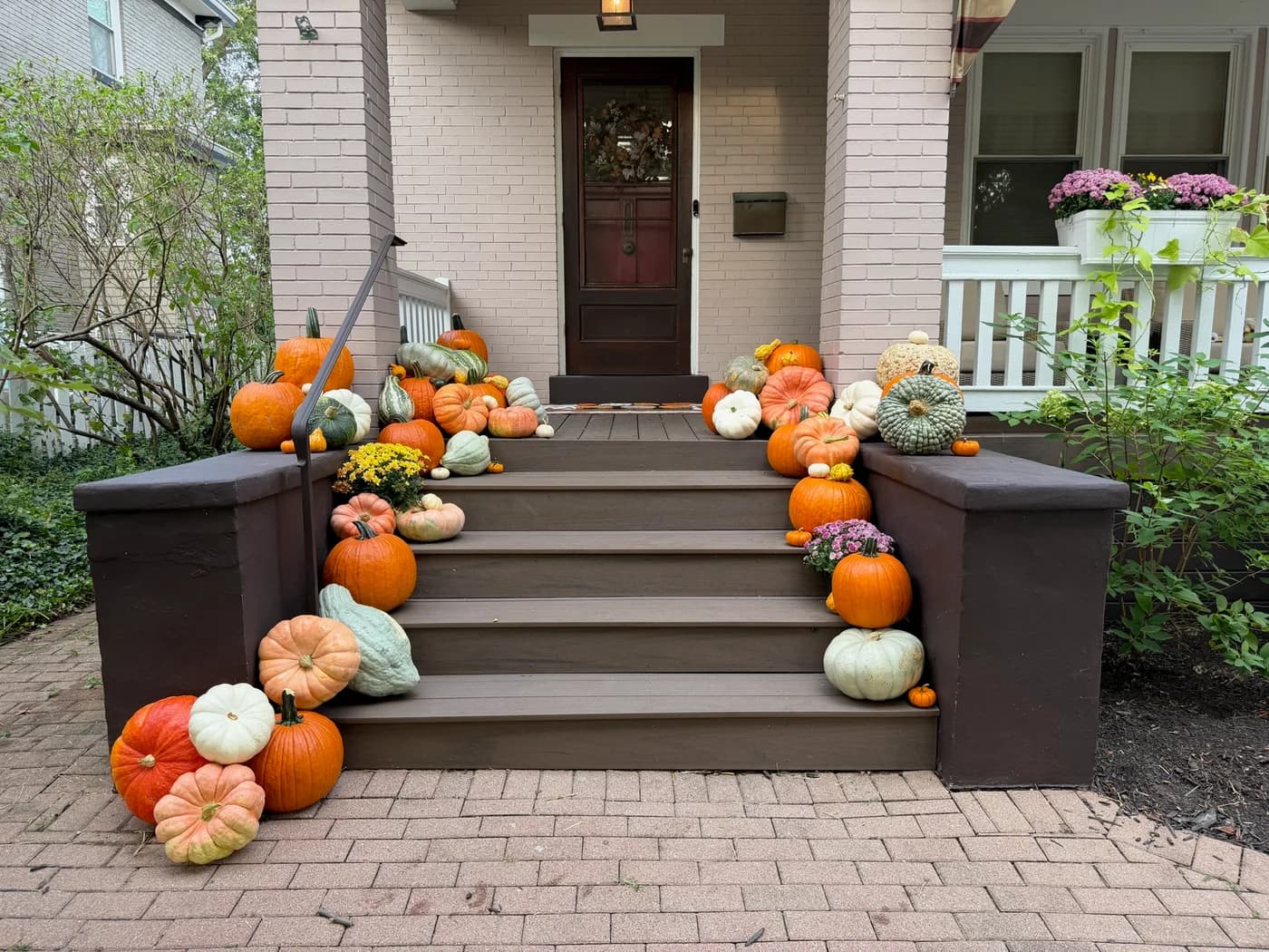 Mixed pumpkins arranged beside the doorway and down both sides of brown porch steps, with the center left open.