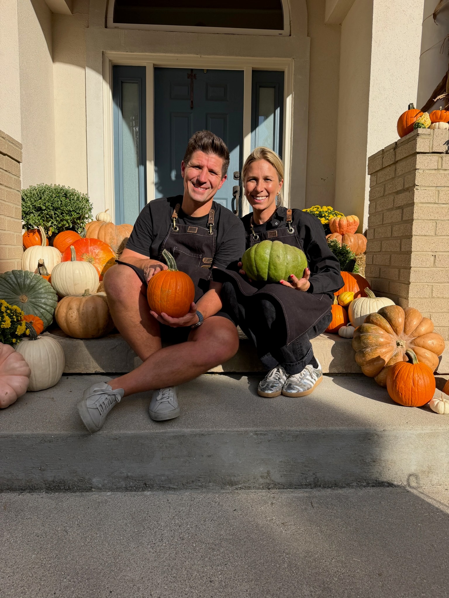 Nikki and Kyle seated on a styled porch with pumpkins and mums